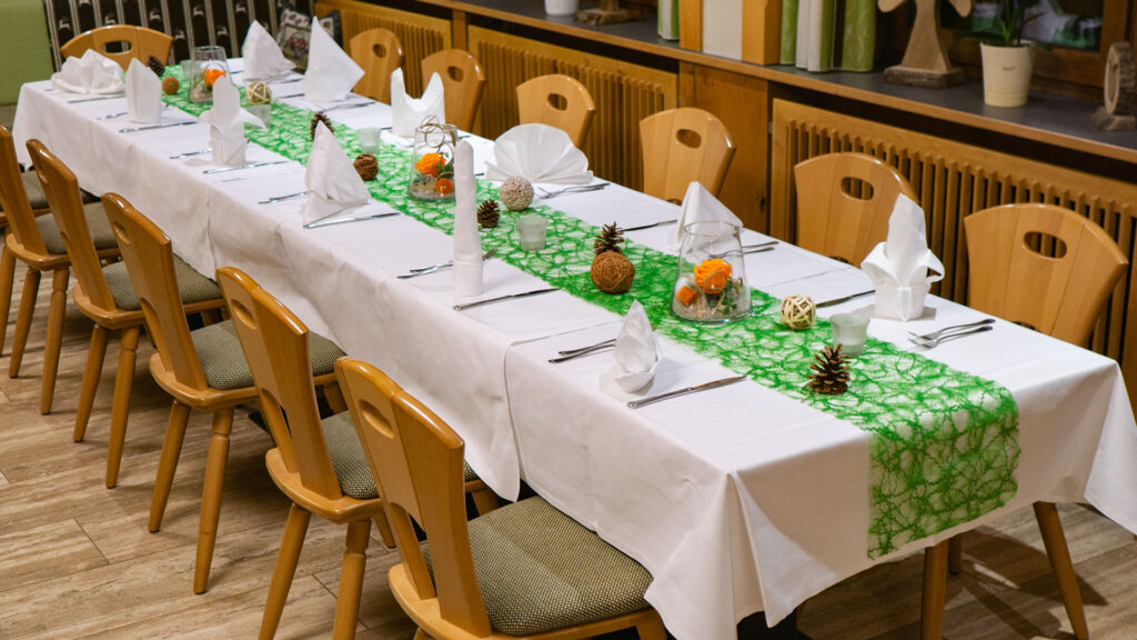 Eine gedeckte Geburtstagstafel mit weißer Tischdecke und grünem Tischläufer. Darauf befinden sich unterschiedlich gefaltene Servietten, Tannenzapfen als Dekoration und Besteck